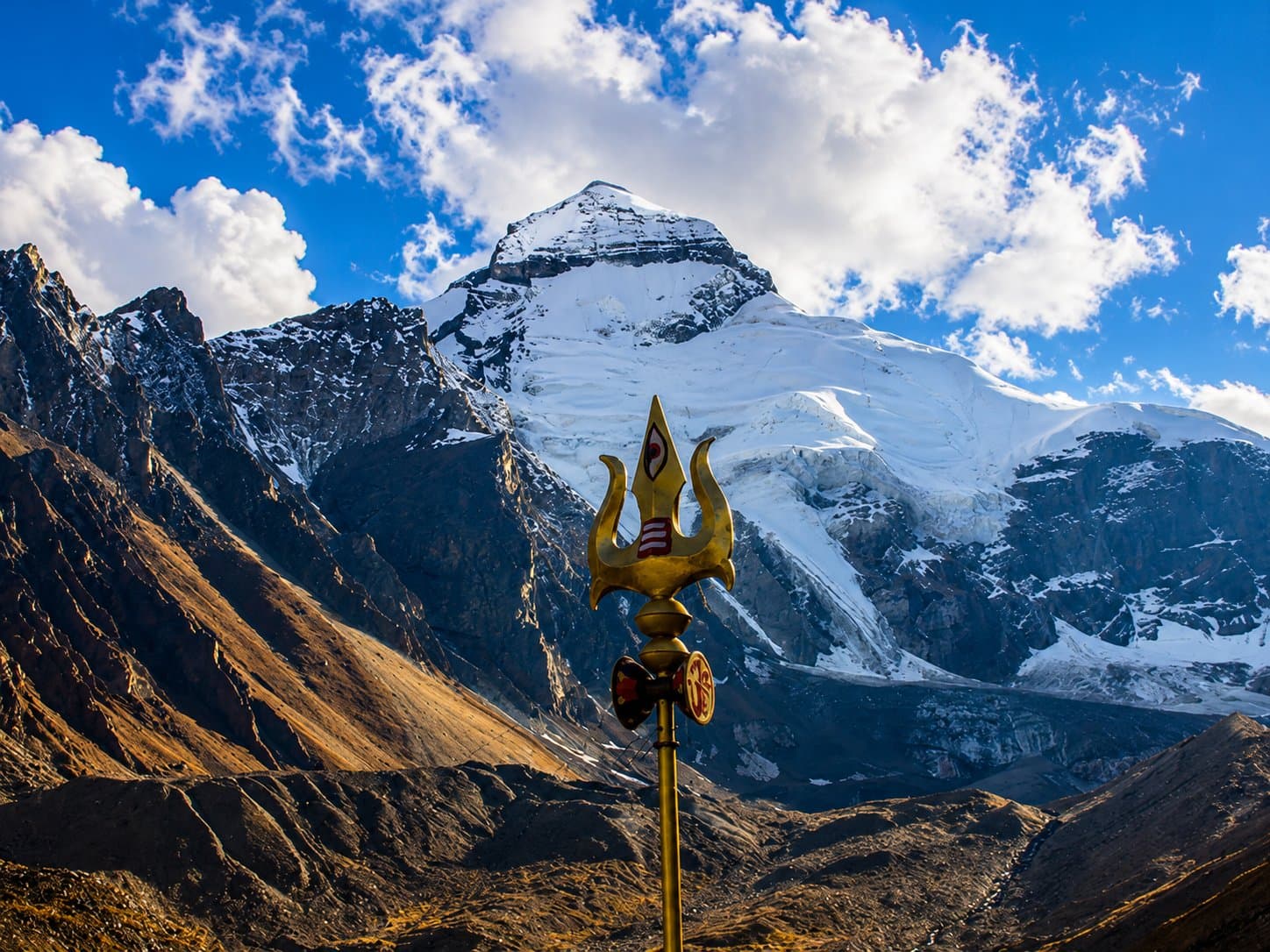 A golden trishul with the snow-capped Adi Kailash peak behind