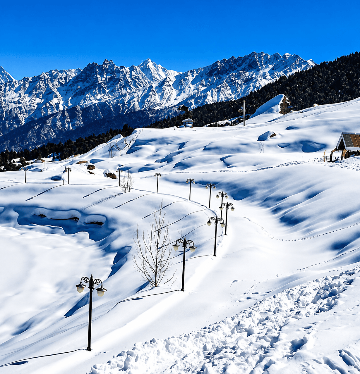Snow-covered Auli slope lined with lamp posts, with the Garhwal Himalayan peaks behind
